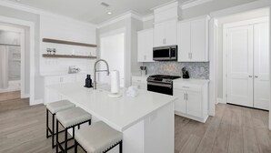 Une cuisine moderne avec des meubles blancs, un îlot central doté de tabourets, un four à micro-ondes et une cuisinière.