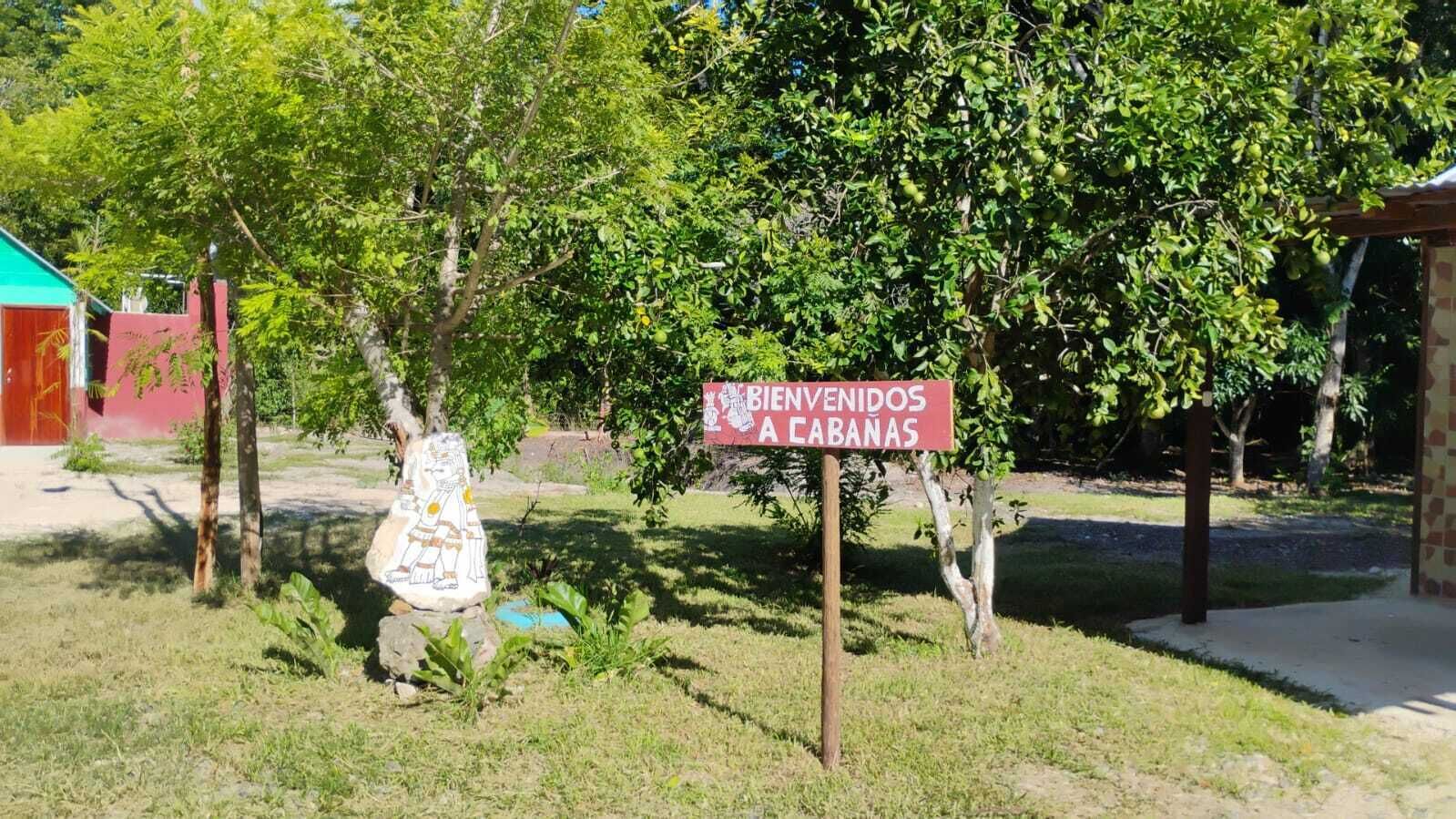 A sign welcoming visitors to a location with a statue and lush greenery.