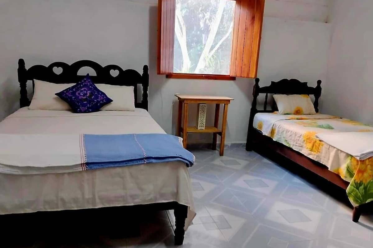 A bedroom with two beds, a small wooden table, and a window with a view of trees.