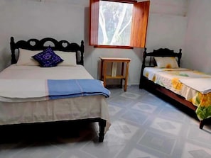 A bedroom with two beds, a small wooden table, and a window with a view of trees.