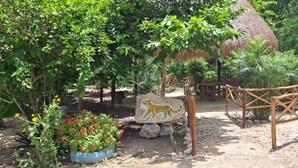 A naturalistic garden with a thatched-roof structure, a wooden bridge, and a painted rock with a leopard design. - Koten Naj (Calakmul)