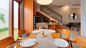 Un coin repas avec une table en bois dressée pour quatre personnes, un escalier et une cuisine en arrière-plan.