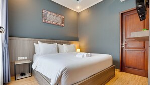 Un lit bien fait, avec du linge de lit blanc et une tête de lit, une table de chevet avec une lampe et une porte en bois.