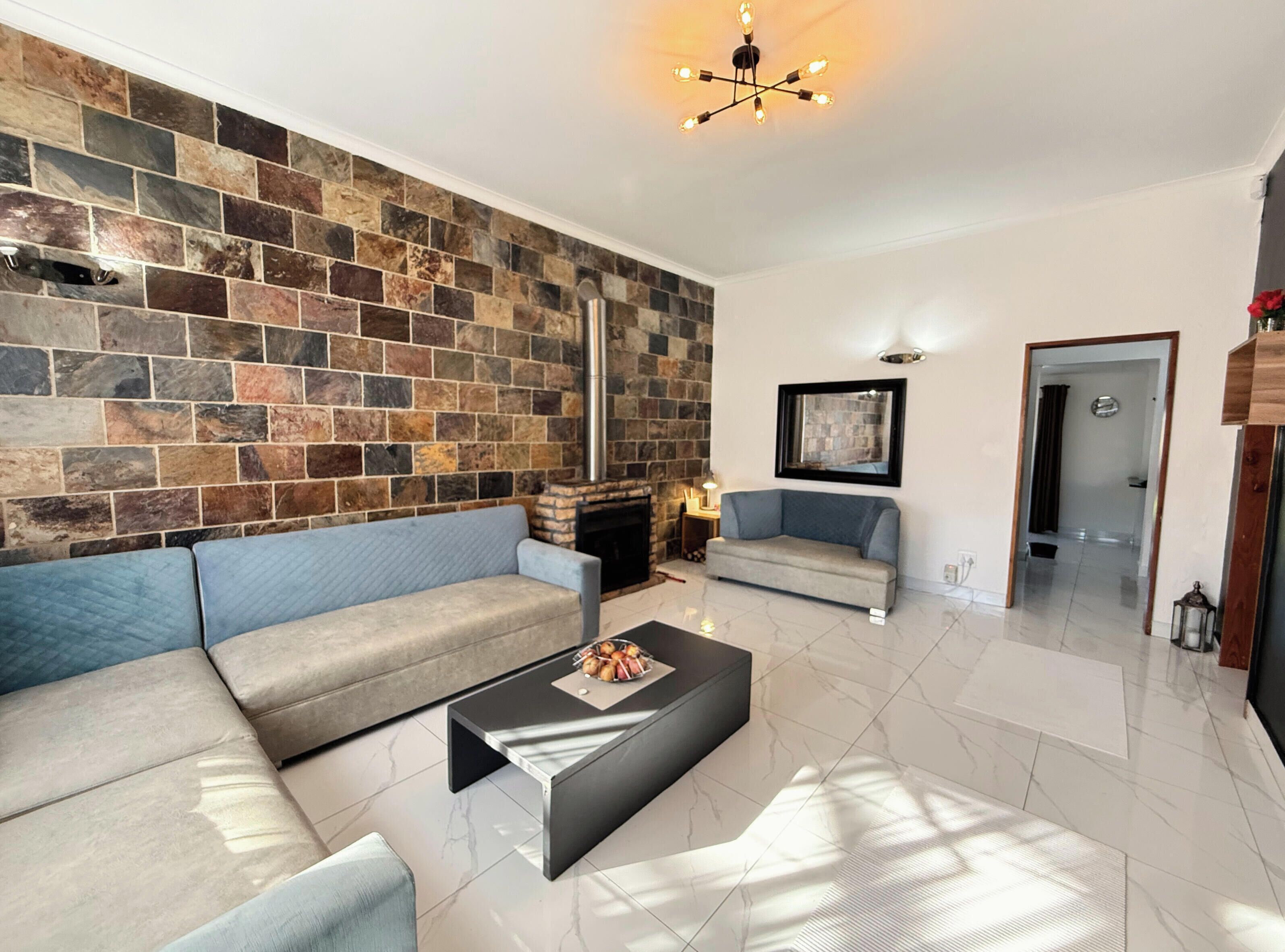 Een woonkamer met een stenen muur, een open haard, een bank, een bijzettafeltje en een moderne lamp.