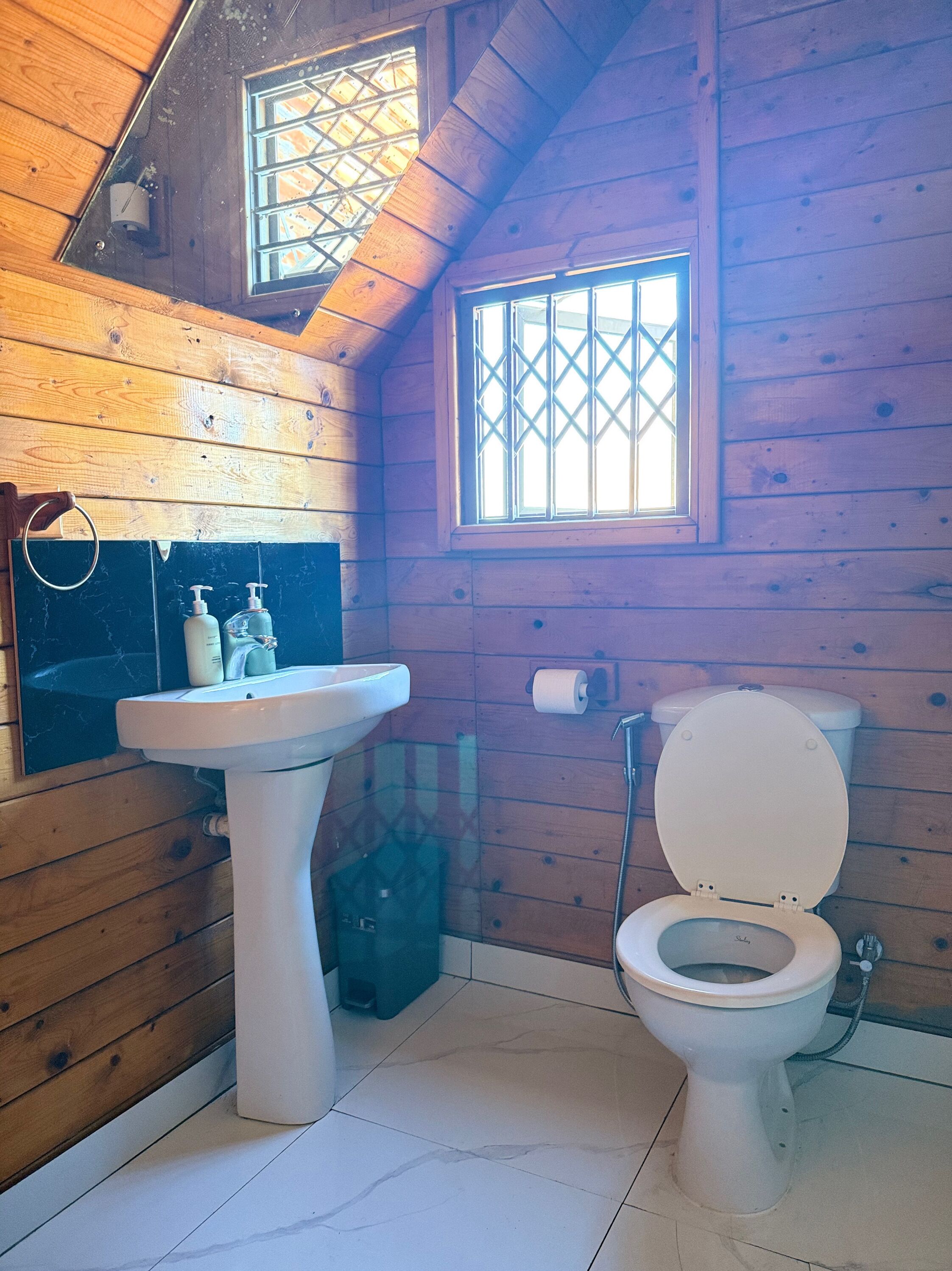 A small, wooden-paneled bathroom with a sink, toilet, and window.