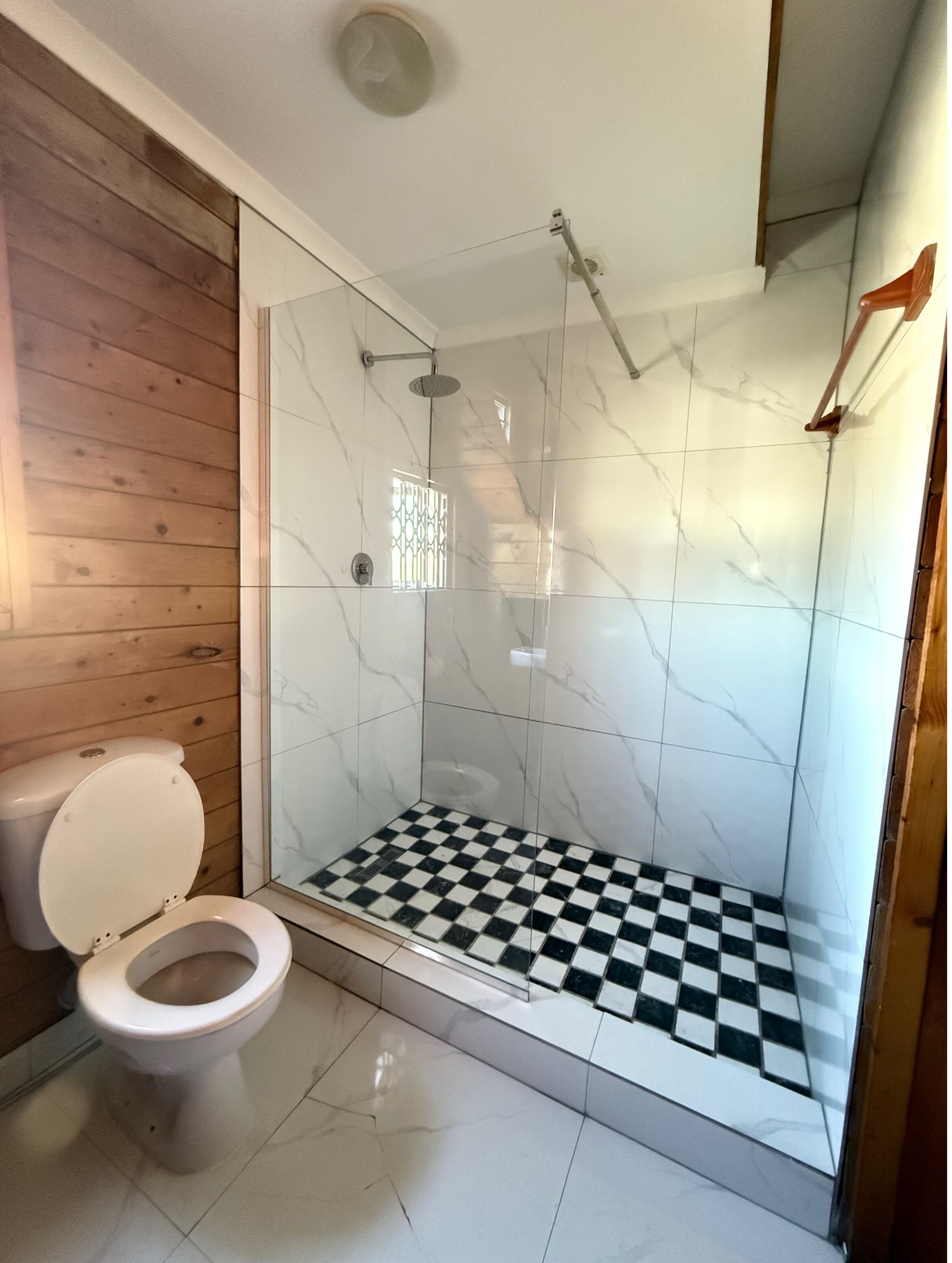 A bathroom with a wooden wall, a white toilet, and a checkered shower floor.