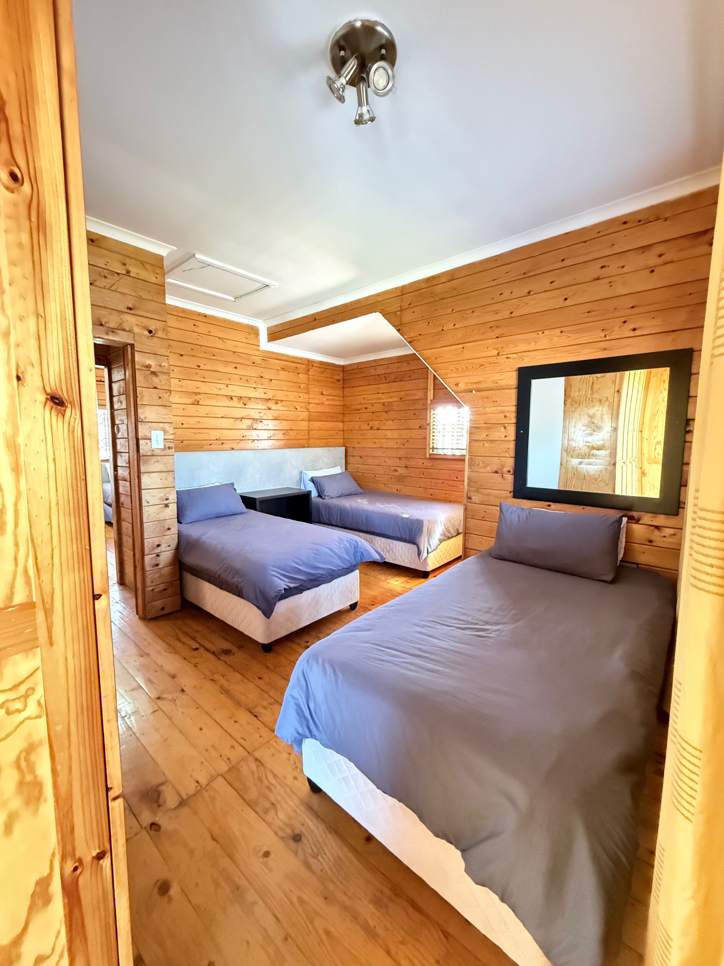 Ein schlicht eingerichtetes Schlafzimmer im Chalet-Stil mit drei Betten, Holzwänden und einer Deckenleuchte.