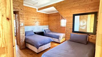 Ein schlicht eingerichtetes Schlafzimmer im Chalet-Stil mit drei Betten, Holzwänden und einer Deckenleuchte.