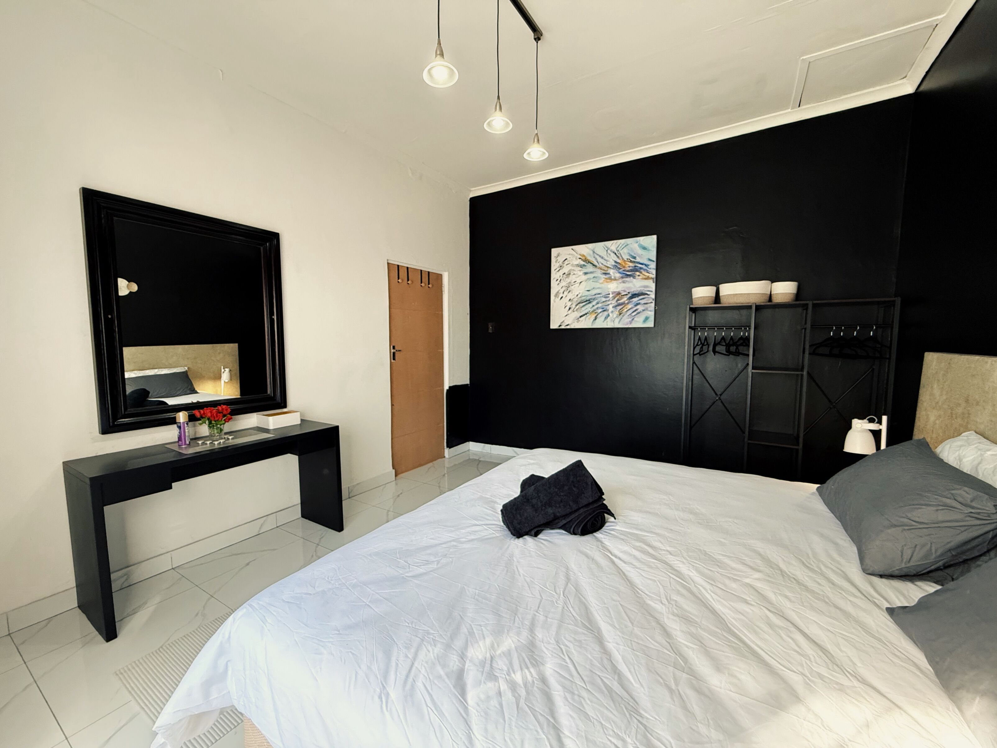 A modern bedroom with a large bed, a black desk, a mirror, and a painting on the wall.