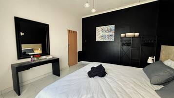 A modern bedroom with a large bed, a black desk, a mirror, and a painting on the wall.