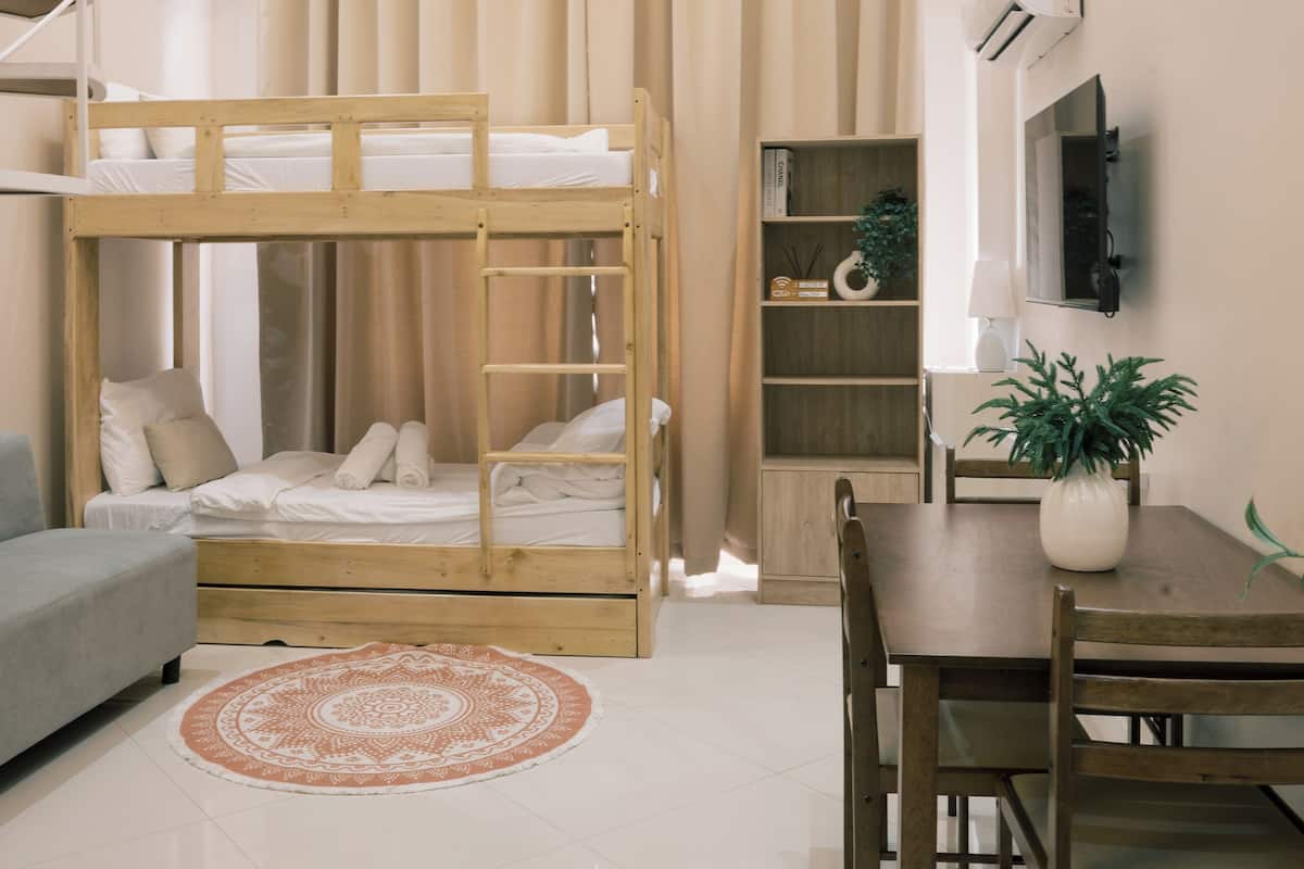 A bunk bed with a ladder, a grey sofa, a wooden table with chairs, a potted plant, and a bookshelf.
