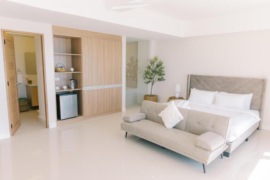 A modern bedroom with a bed, a sofa, a small refrigerator, and a wardrobe.
