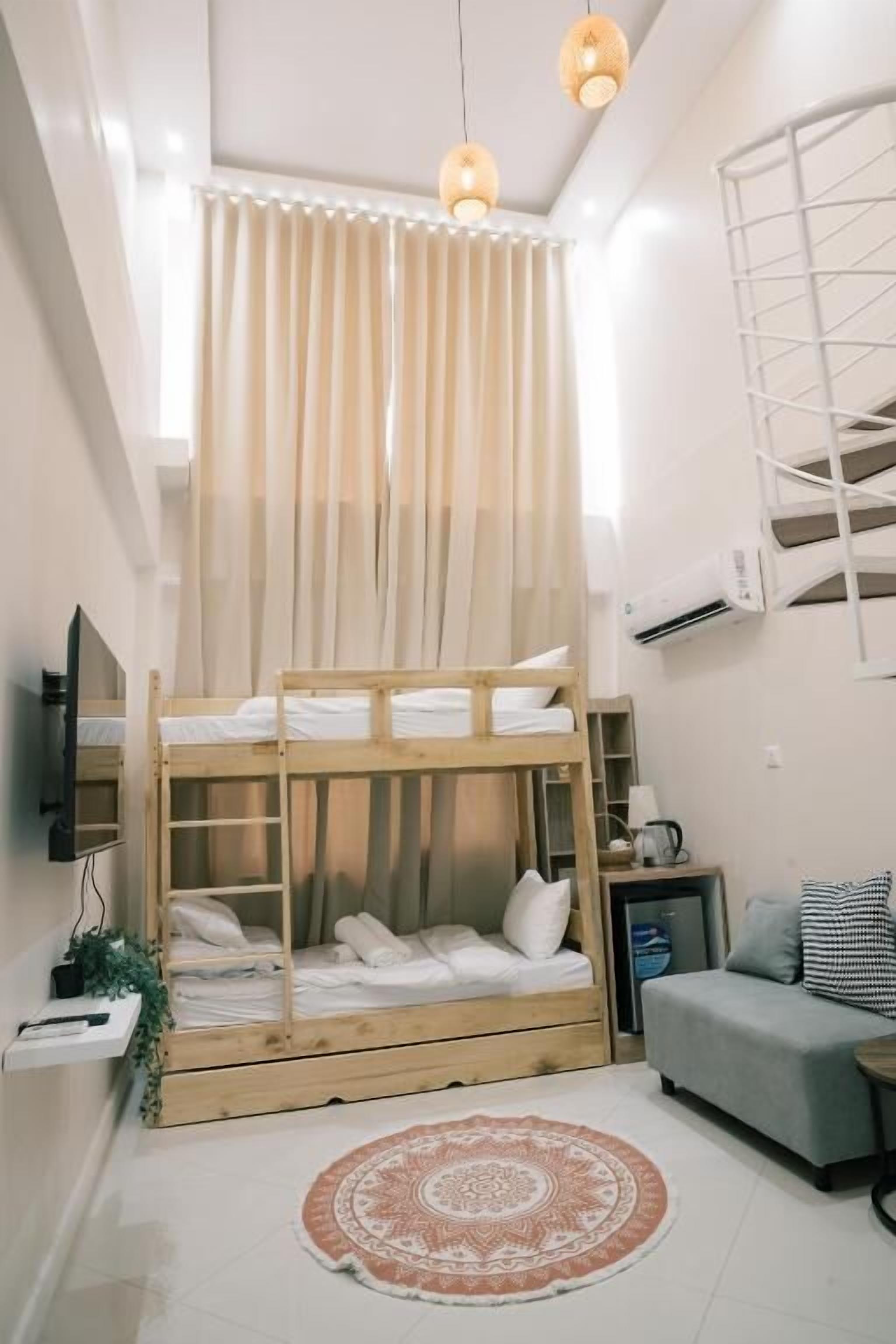 A compact room with a bunk bed, a small sofa, a round rug, and a TV on a shelf.