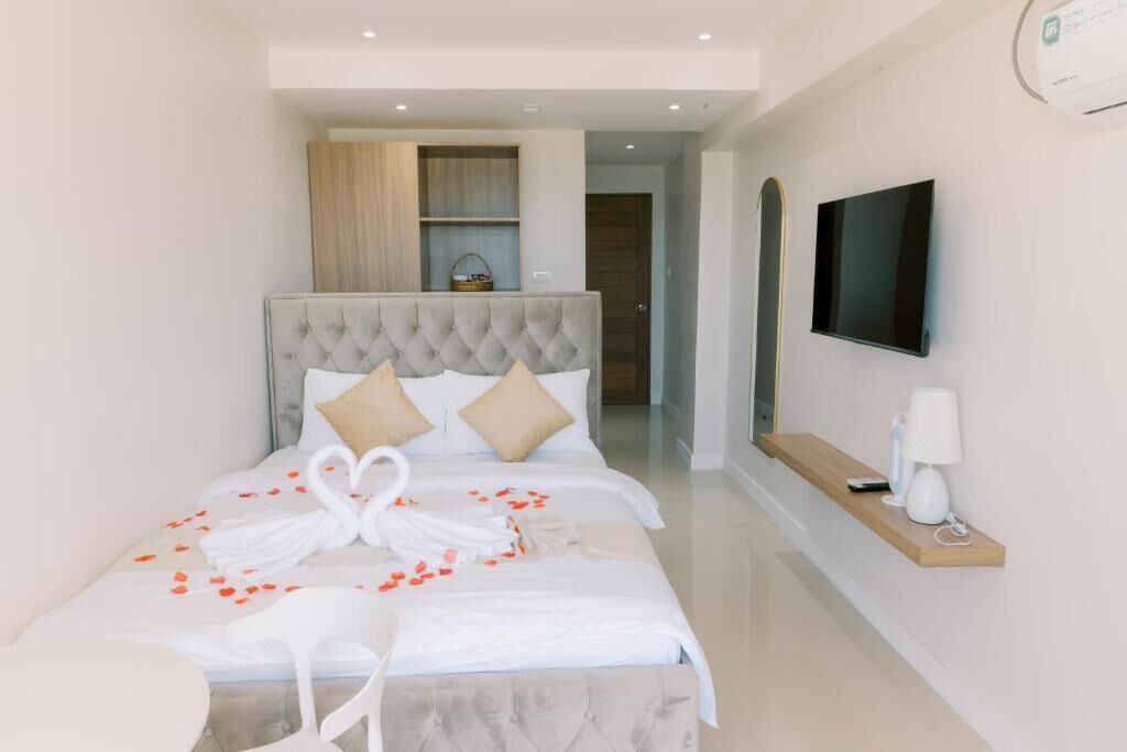 Une chambre d’hôtel moderne avec une tête de lit capitonnée, un téléviseur à écran plat, une table de chevet avec une lampe et un cygne décoratif posé sur le lit.