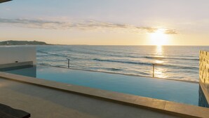 An infinity pool with a view of the ocean and sunset. - Palms La Union Suites (San Juan)