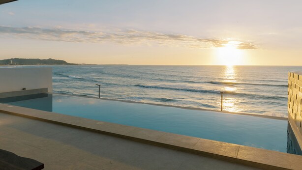Une piscine à débordement offrant une vue sur l’océan et le coucher de soleil.