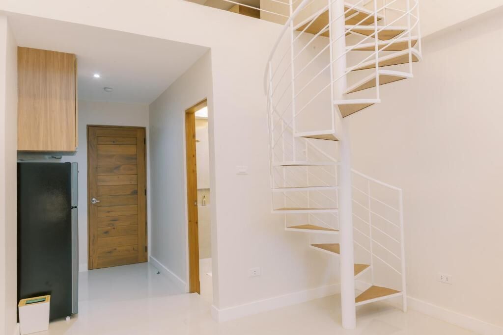 A modern interior with a spiral staircase, a wooden door, and a black refrigerator.
