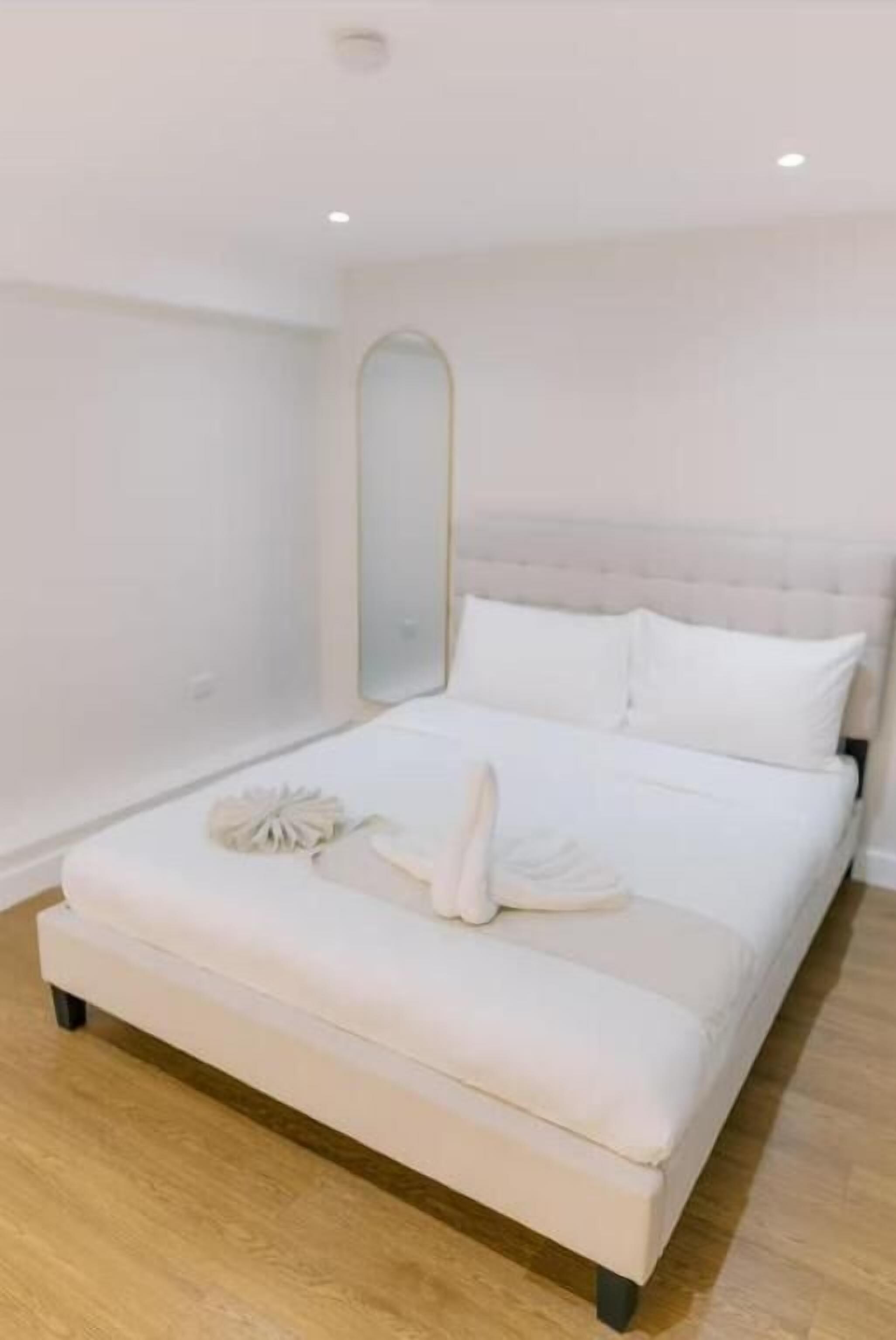 A bedroom with a large bed, a mirror, and a wooden floor.