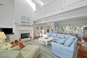 A spacious living room with a large sectional sofa, a fireplace, and a dining area with white chairs. - A Watercolor is an oceanfront 4BR/3BA retreat located on the beach (Bald Head Island)