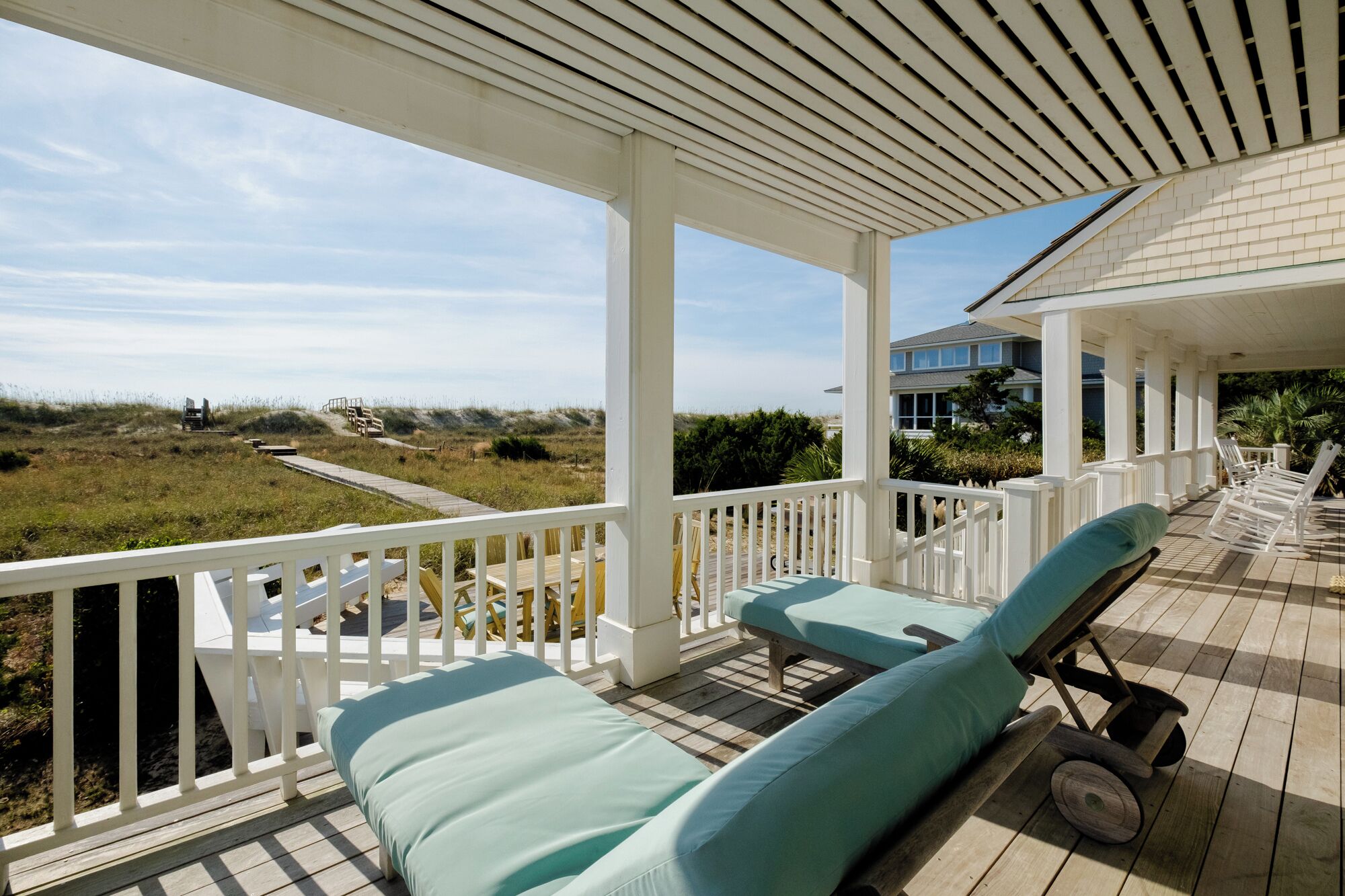A covered outdoor area with a wooden deck, white railings, and two lounge chairs with cushions.