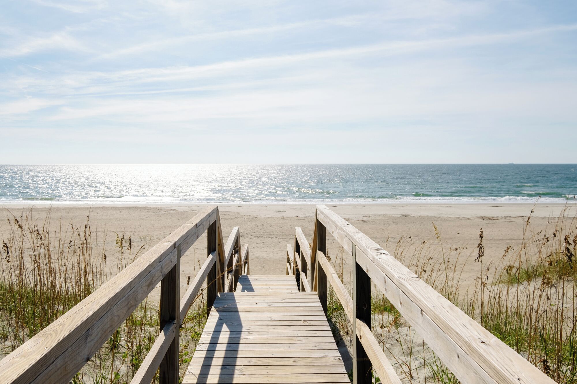 Une promenade en bois menant à une plage de sable et d’algues.
