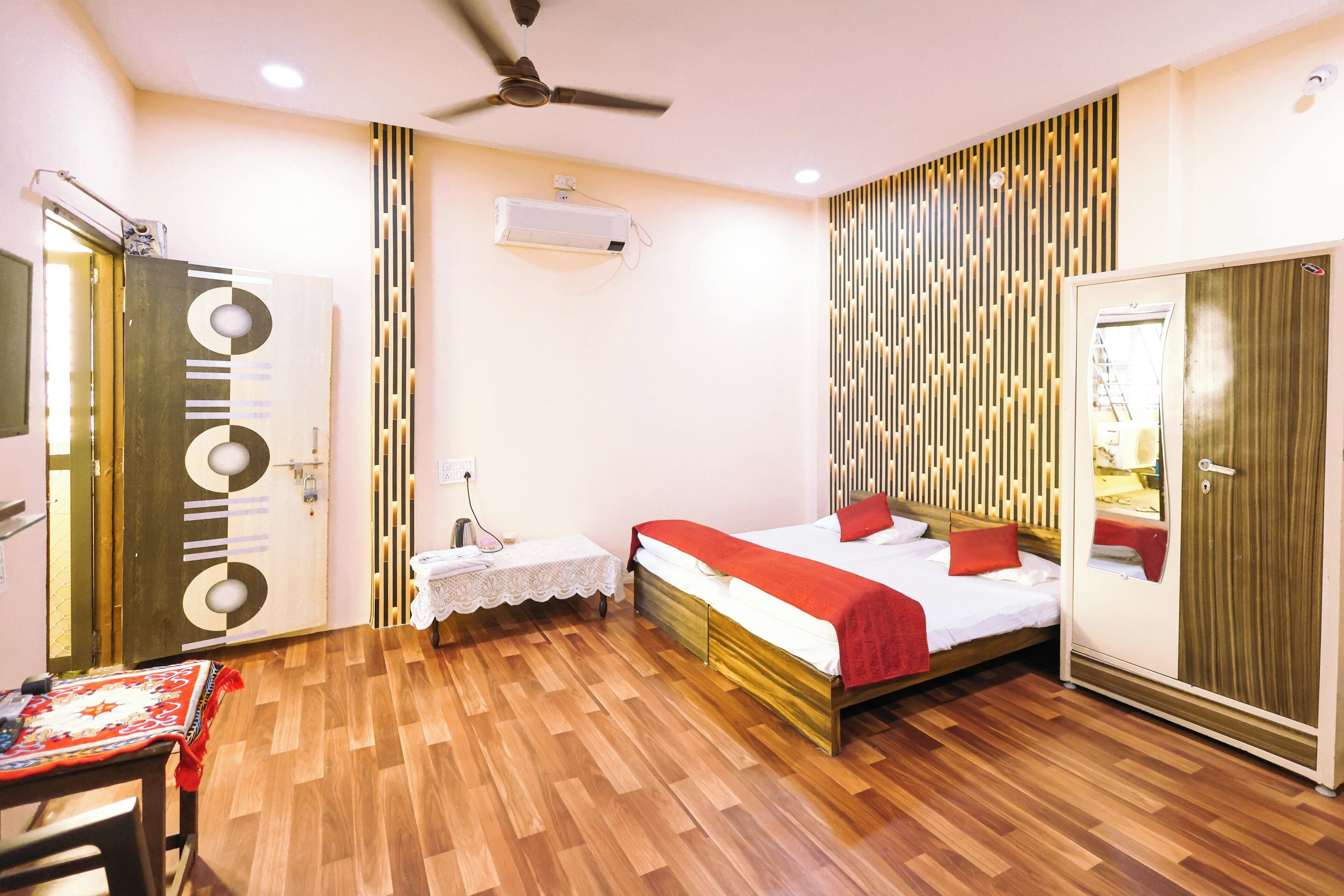 A bedroom with a bed, a desk, and a chair. There is a ceiling fan and an air conditioning unit.