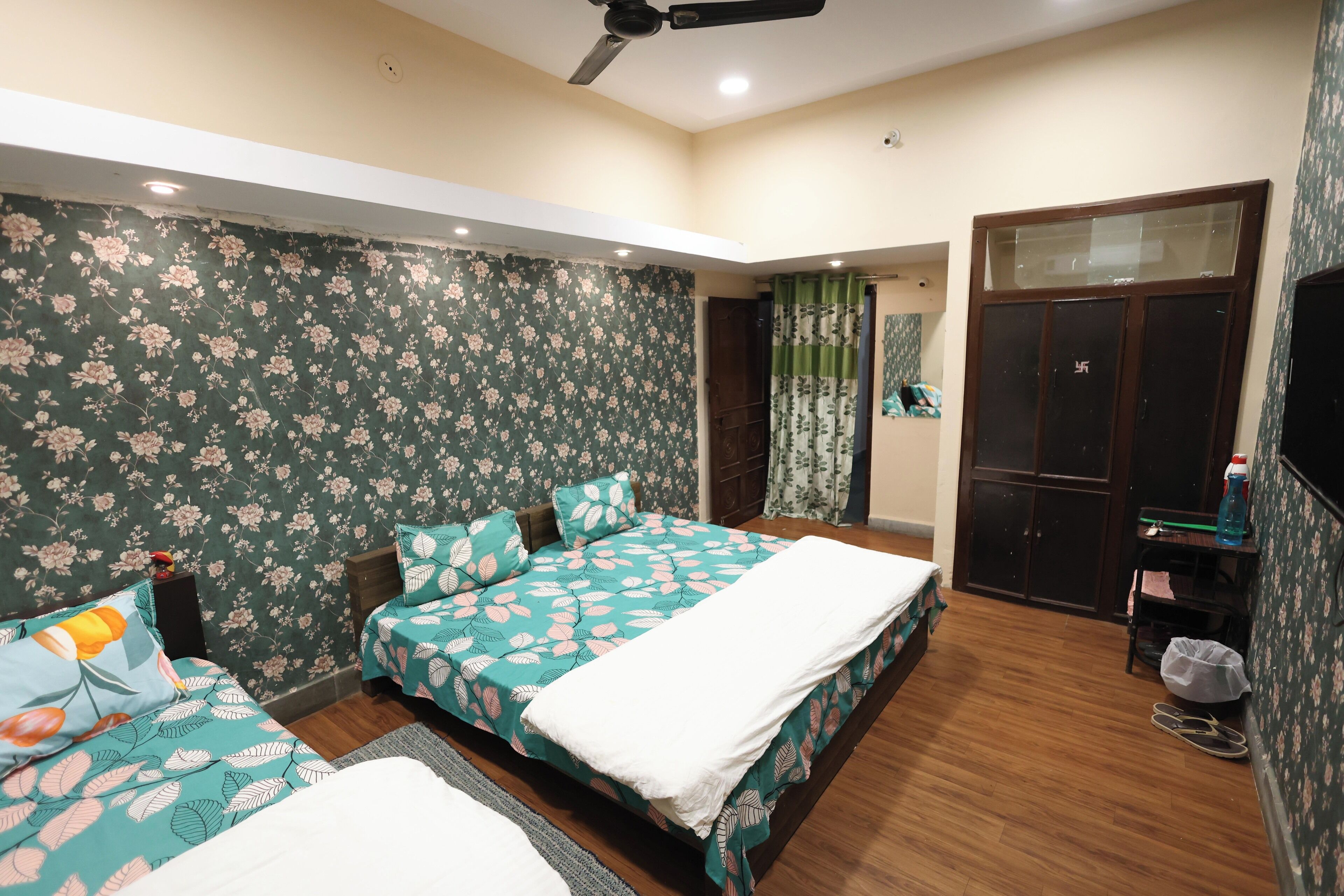 A bedroom with two beds, floral wallpaper, a ceiling fan, and a wardrobe.