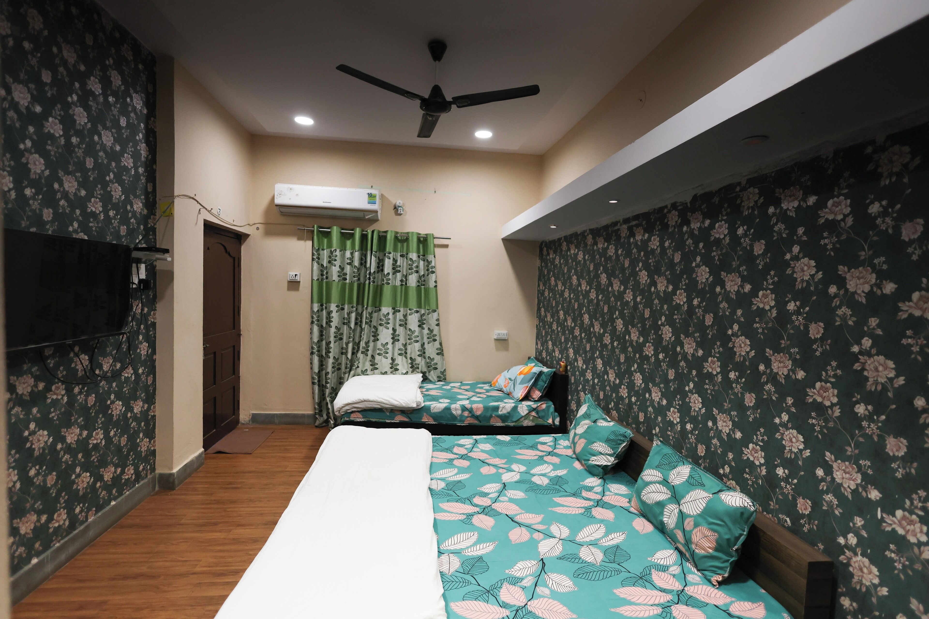 A bedroom with two single beds, a ceiling fan, an air conditioning unit, and floral wallpaper.