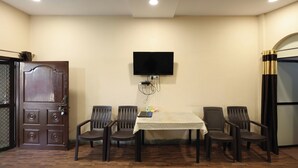 A conference room with a table, chairs, a TV mounted on the wall, and a door with a decorative panel. - Dream Homestay (Ujjain)
