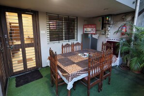 A dining area with a wooden table and chairs, a 'No Smoking' sign, a fire extinguisher, and a window with blinds. - Dream Homestay (Ujjain)