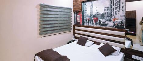 A neatly made bed with a patterned bedspread, a large window with blinds, and a painting of a cityscape on the wall.
