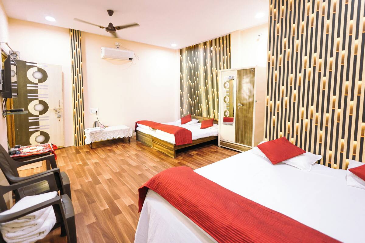 Une chambre d’hôtel avec un plancher en bois, deux lits avec une literie rouge et blanche, un ventilateur de plafond, un miroir et un mur avec des lambris en bois verticaux.