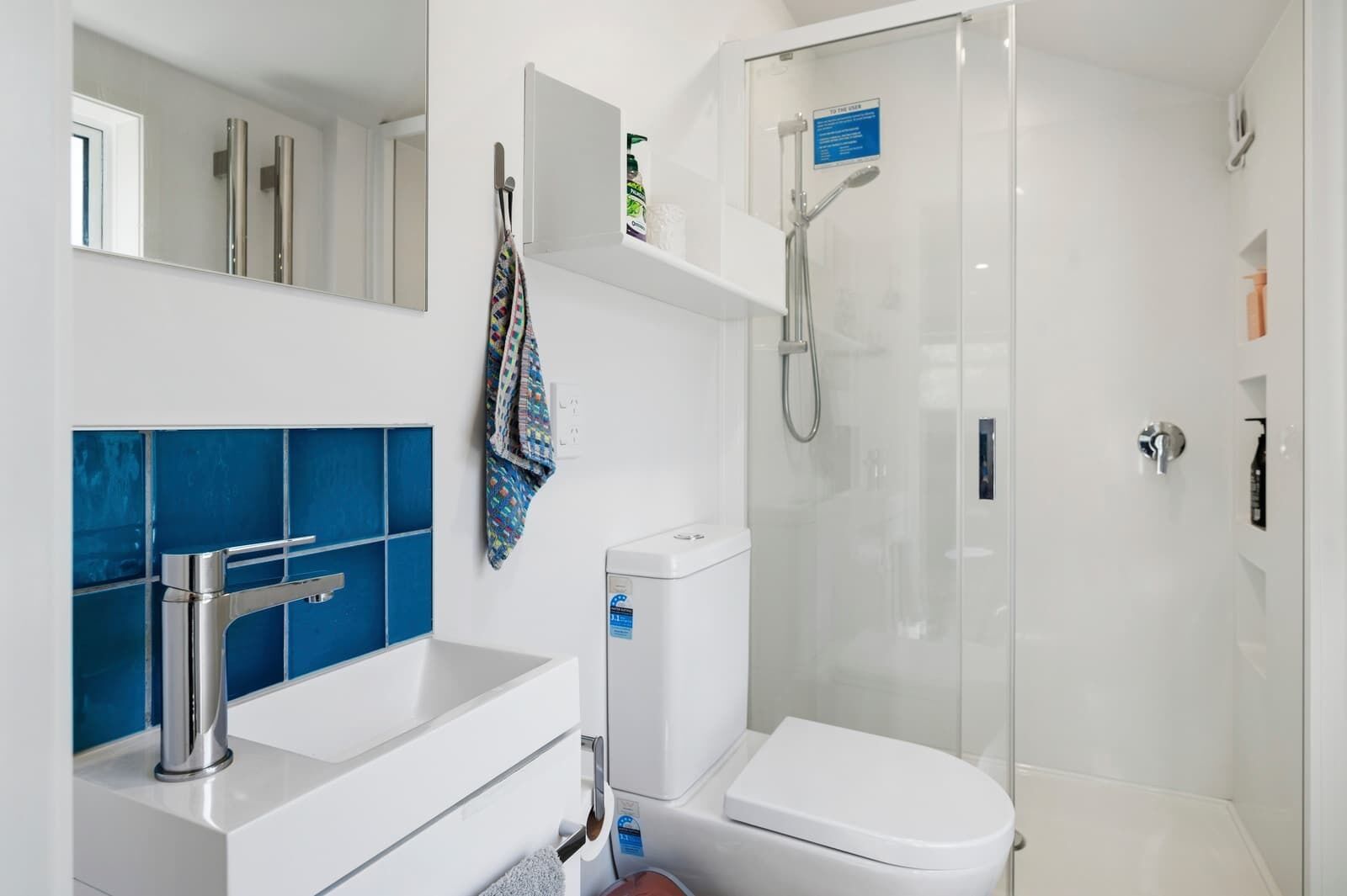 A modern bathroom with a glass-enclosed shower, a white sink with a chrome faucet, and a blue-tiled vanity.