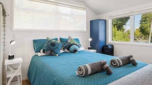 Un dormitorio con una cama grande, dos lámparas de noche, un armario azul y una ventana con vistas a zonas verdes.