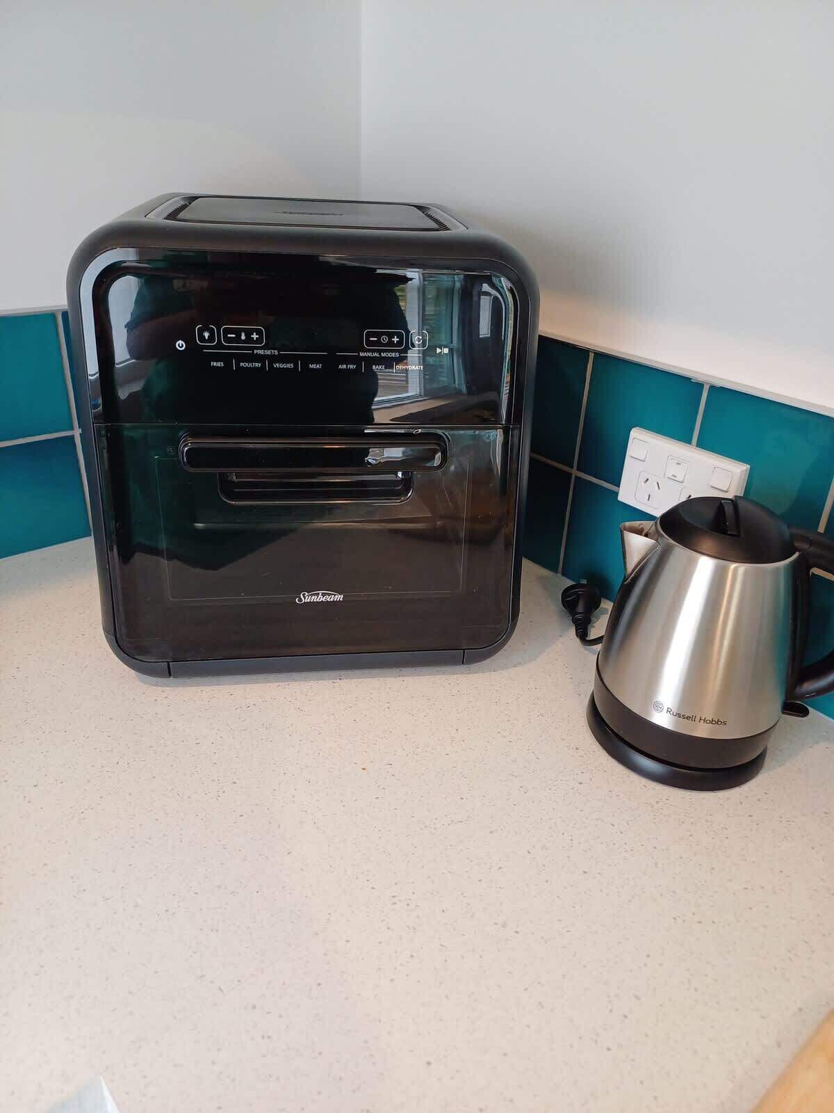 A black toaster with a digital display and multiple preset buttons on a kitchen counter next to a kettle.