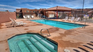 A swimming pool with lounge chairs and a covered area, surrounded by a fence and buildings. - Easy, comfortable stay near Moab's best adventures (Moab)