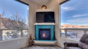 A living room with a fireplace, a flat-screen TV above it, and a view of the outdoors through large windows. - Easy, comfortable stay near Moab's best adventures (Moab)