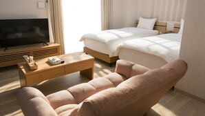 Quarto de hotel com televisão de tela plana, sofá, cama com duas almofadas, mesa de cabeceira e janela com cortinas.