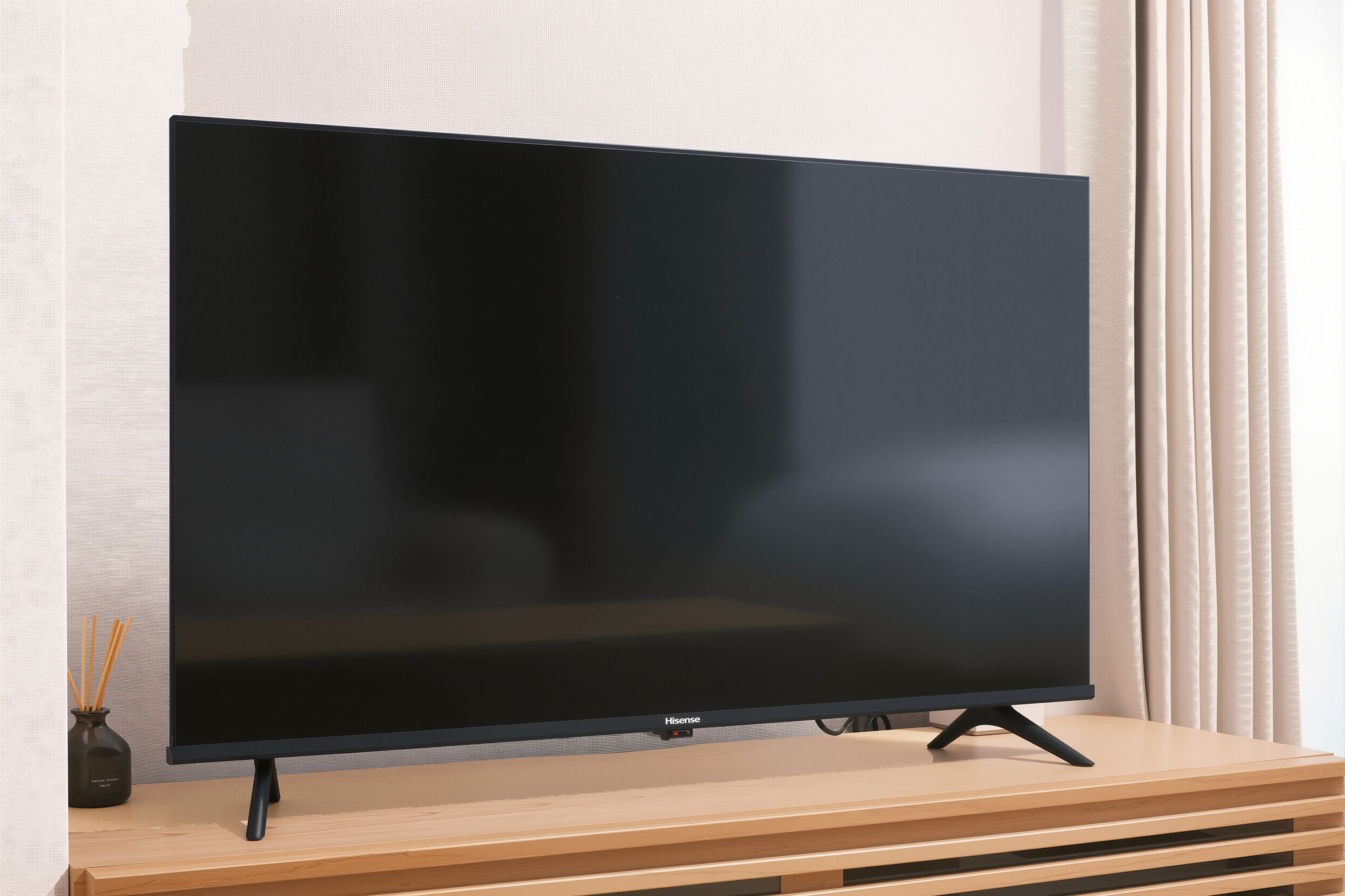Un téléviseur à écran plat, posé sur un meuble en bois, avec une télécommande, est placé contre un mur orné de rideaux.