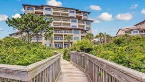 Un hotel de varios pisos con balcones, un paseo de madera y abundante follaje.