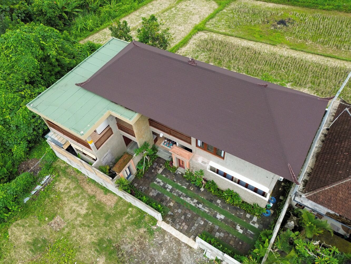 An aerial view of a building with a flat roof, surrounded by greenery and adjacent fields.