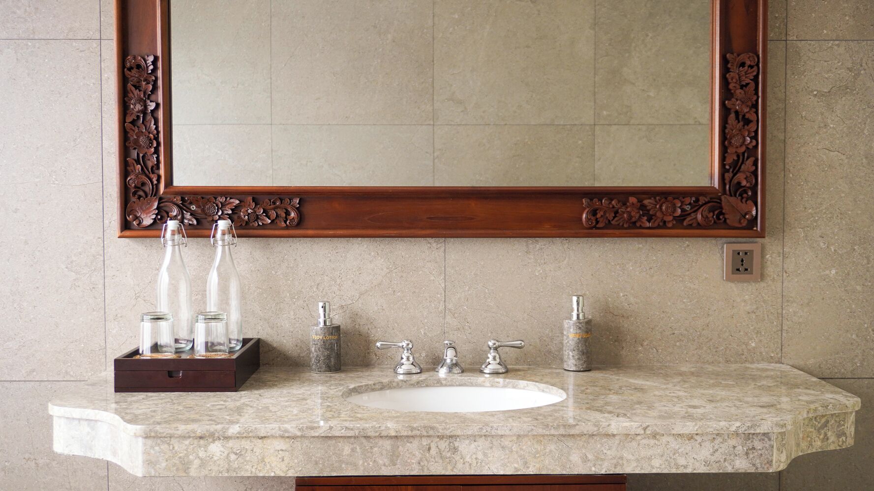 Une salle de bain avec un lavabo en marbre, deux robinets et un grand miroir encadré d’un cadre en bois ouvragé.