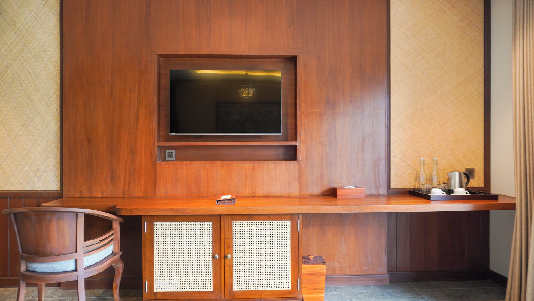 Un escritorio de madera con un televisor, una silla y un mueble bajo con frente perforado.