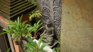 A stone Buddha statue in a garden setting with a stone wall featuring floral carvings. - Naata Villas Ubud (Sukawati)