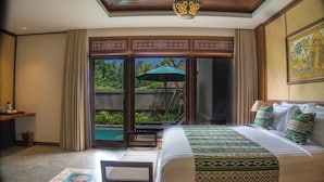 A hotel room with a large bed, a desk, and a view of a garden through glass doors. - Naata Villas Ubud (Sukawati)