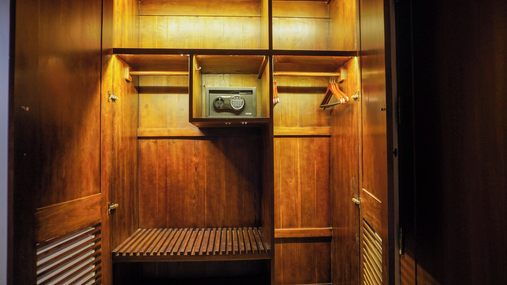 Un placard en bois avec des étagères et une tringle à vêtements, un petit banc en bois et un objet encadré accroché au mur.
