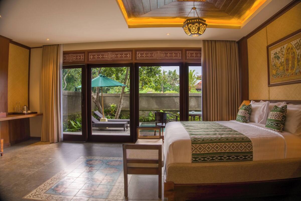 Quarto de hotel com cama grande, escrivaninha e vista para um jardim através de portas de correr.