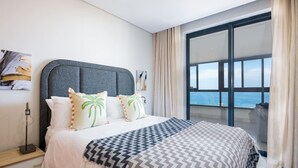 Habitación de hotel con una cama grande, vista al mar y un balcón con cortinas.