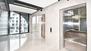 Een moderne lift met glazen deur, bedieningspaneel en een bordje met de verdiepingen.