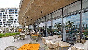 Een terras met rieten meubels en een houten tafel, met uitzicht op een stadsgezicht.